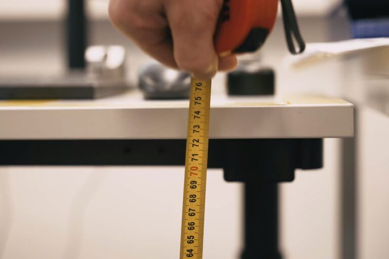 Ergonom měří svinovacím metrem výšku pracovní plochy